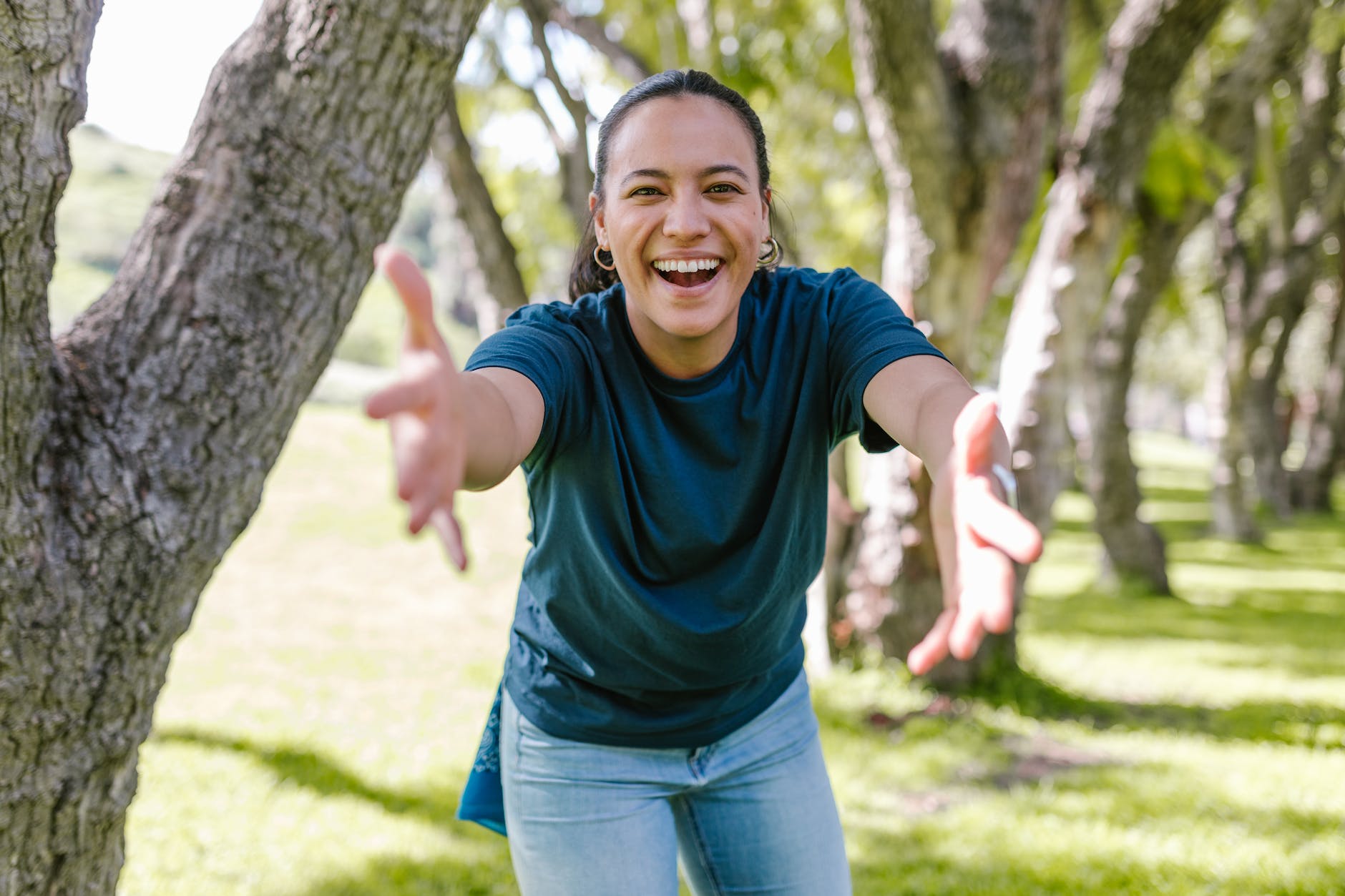 Mulher jovem com um sorriso no rosto e de braços abertos para acolher você.